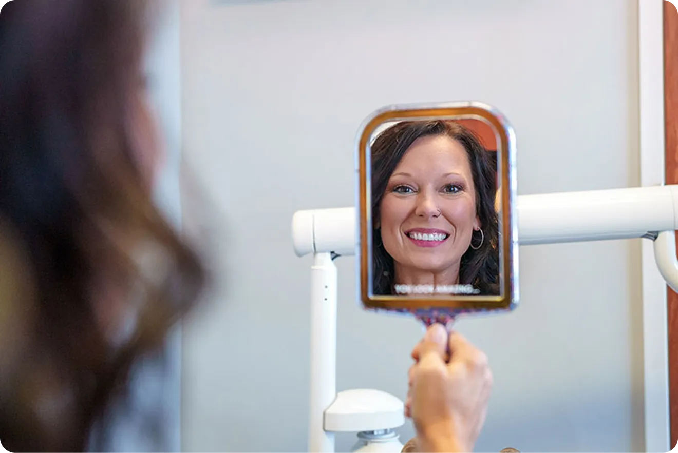 Patient admiring her final smile in a mirror after dental implant restoration